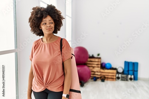 African american woman with afro hair holding yoga mat at pilates room smiling looking to the side and staring away thinking.