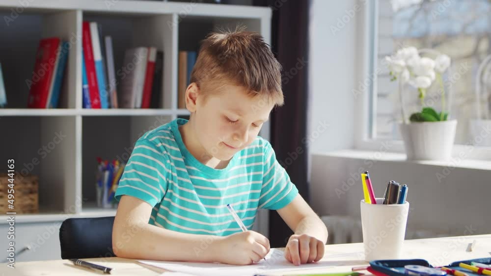 Boy is Doing his Homework at the Table. Cute Child is Learning at Home with the Help of Textbooks and School Materials. Study and Education Concept. Boy is Doing his Homework at the Table. Cute Child is Learning at Home with the Help of Textbooks and School Materials. Study and Education Concept.