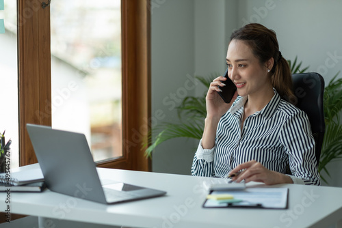Young accountant hand holding smartphone to call marketing consultants and using laptop computer to analyze sales growth in the global workplace market. accounting concept