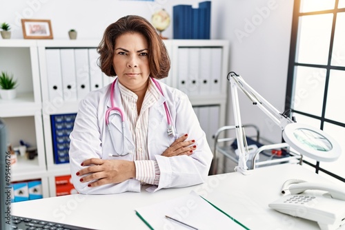 Middle age hispanic woman wearing doctor uniform and stethoscope at the clinic skeptic and nervous, disapproving expression on face with crossed arms. negative person.