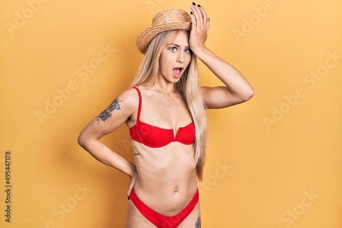 Young caucasian woman wearing bikini and summer hat surprised with hand on head for mistake, remember error. forgot, bad memory concept.