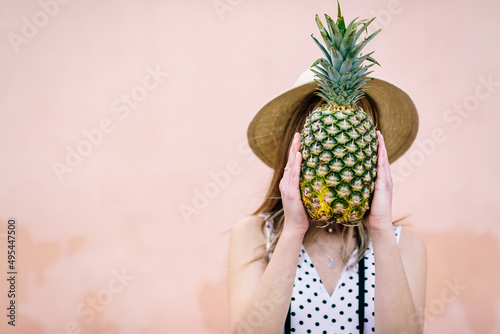 Woman holding pineapple fruit wearing hat against pink background photo