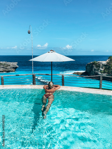 Woman in bikini swimming in infinity pool ocean view in Bali photo