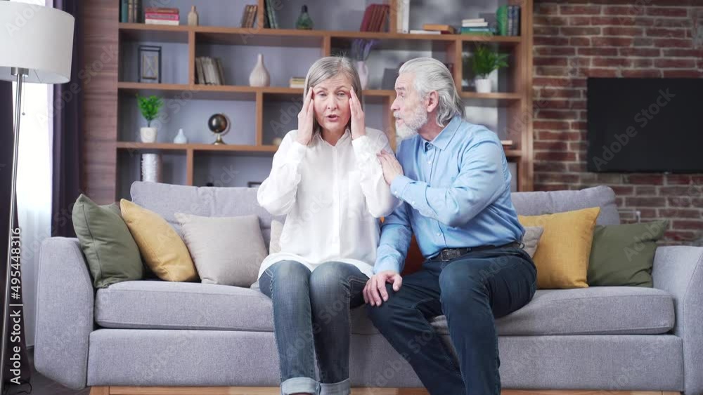 Senior mature man helping her woman with Headache, stress, pain. Old man feeling bad pain disease. Wife supporting husband - Elderly couple suffering migraine depression ache. sitting at home indoors Senior mature man helping her woman with Headache, stress, pain. Old man feeling bad pain disease. Wife supporting husband - Elderly couple suffering migraine depression ache. sitting at home indoors