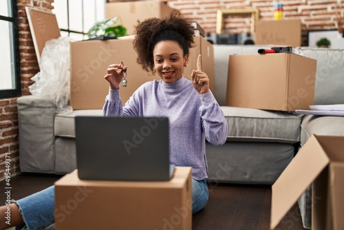 Young african american woman showing keys of new home on video call smiling with an idea or question pointing finger with happy face, number one