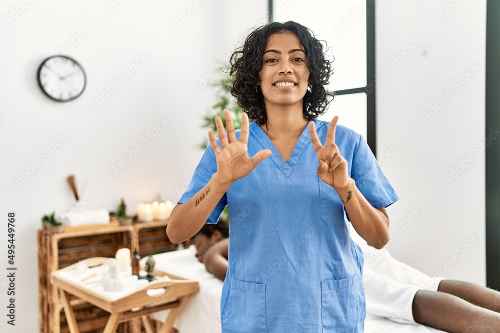 Young therapist woman at wellness spa center showing and pointing up with fingers number seven while smiling confident and happy. Young therapist woman at wellness spa center showing and pointing up with fingers number seven while smiling confident and happy.