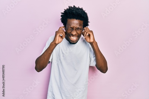 Fotobehang Young african american man wearing casual white t shirt covering ears with fingers with annoyed expression for the noise of loud music