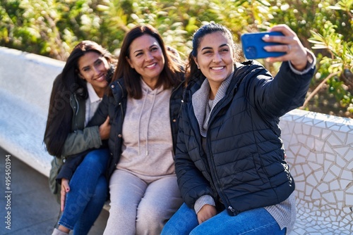 Three woman mother and daughters making selfie by smartphone sitting on bench at park