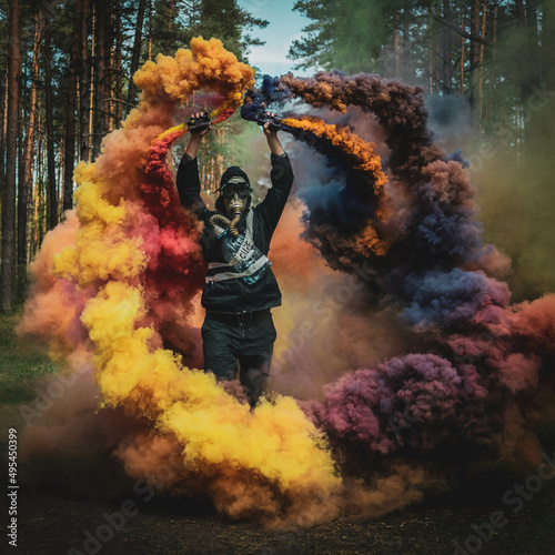 Young man with gas mask holding colorful smoke guns standing in the woods photo