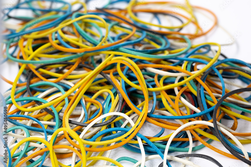 Many colored stationery rubber bands of yellow red blue green colors lie in a heap on a white background office tools