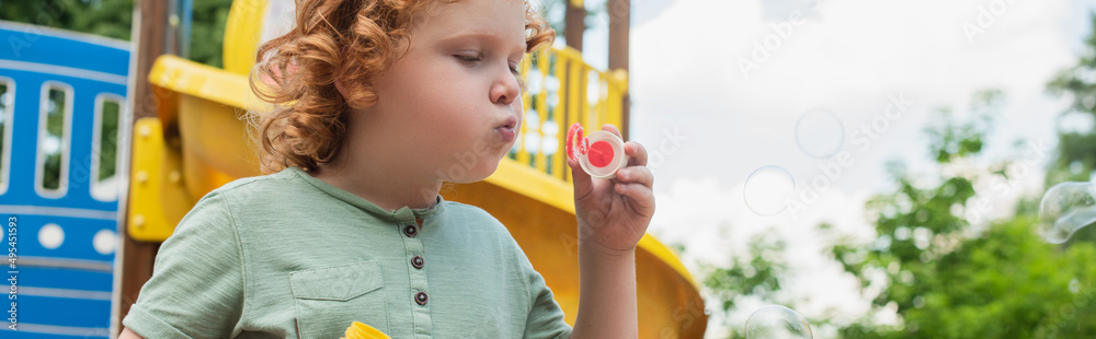 curly boy blowing soap bubbles while spending time outdoors, banner. curly boy blowing soap bubbles while spending time outdoors, banner.