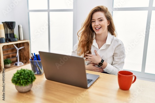 Young caucasian woman working at the office using computer laptop smiling and laughing hard out loud because funny crazy joke with hands on body.