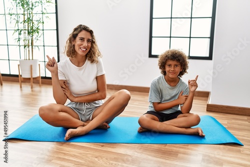 Young woman and son sitting on training mat at the gym smiling happy pointing with hand and finger to the side