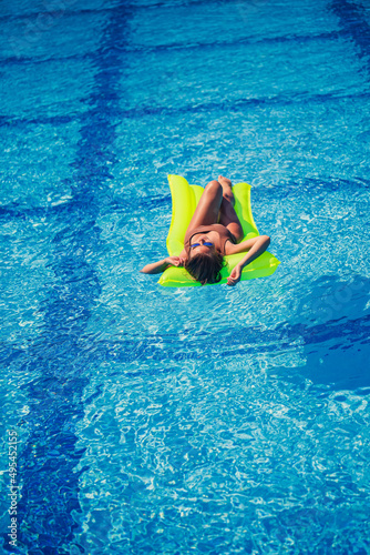 Young sexy wman in a swimsuit swims in the pool on an inflatable mattress. Girl in sunglasses in a blue pool on vacation