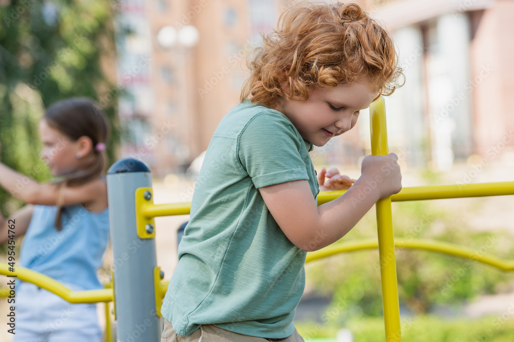 curly boy playing near blurred girl on playground. curly boy playing near blurred girl on playground.