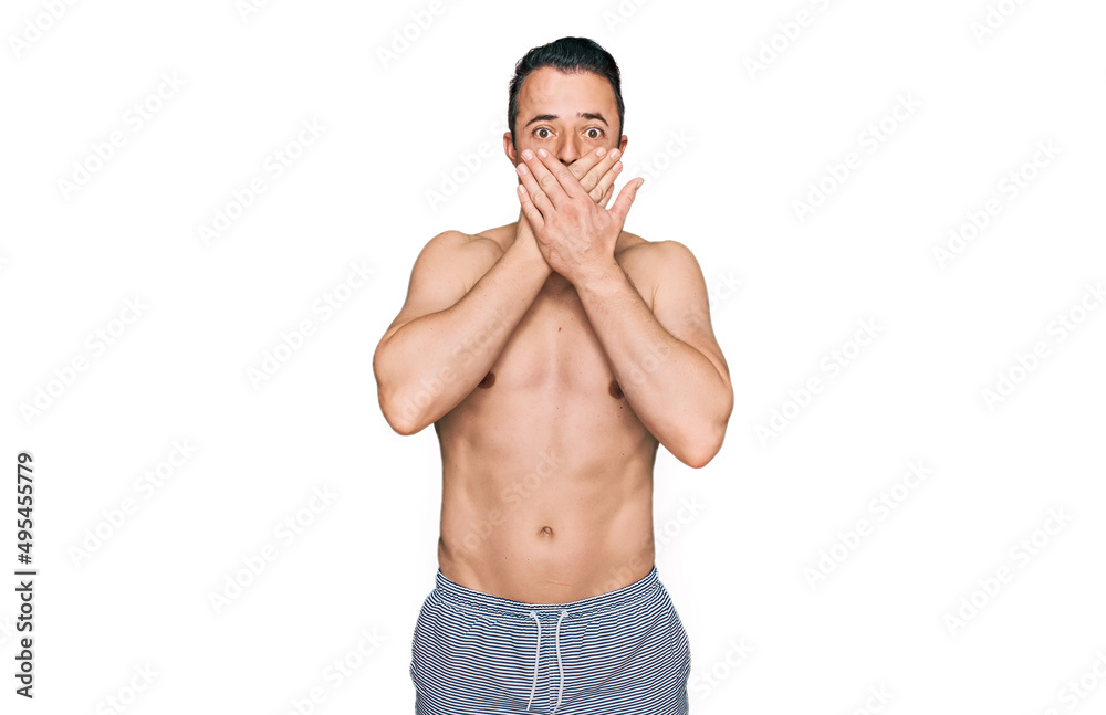 Fototapeta premium Handsome young man wearing swimwear shirtless shocked covering mouth with hands for mistake. secret concept.