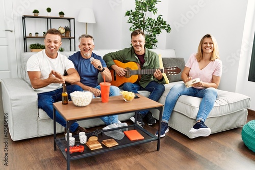 Group of middle age friends on party singing and playing guitar at home.