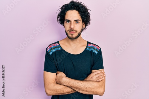 Handsome hispanic man with arms crossed gesture relaxed with serious expression on face. simple and natural looking at the camera.