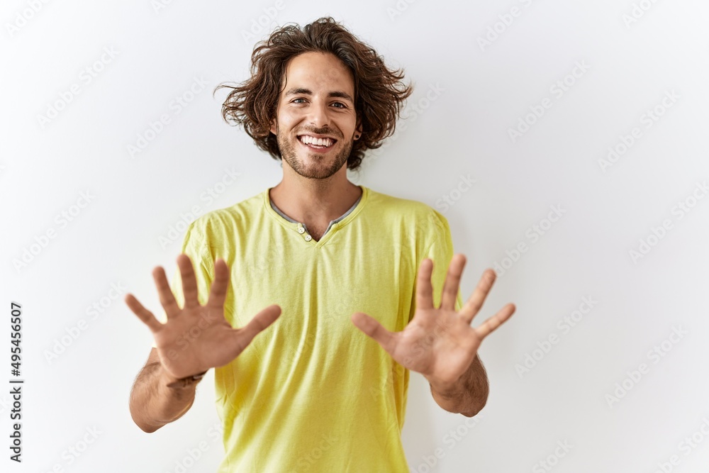 Young hispanic man standing over isolated background showing and pointing up with fingers number ten while smiling confident and happy.