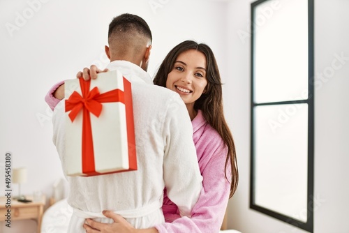 Young hispanic couple smiling happy surprising with gift at bedroom.