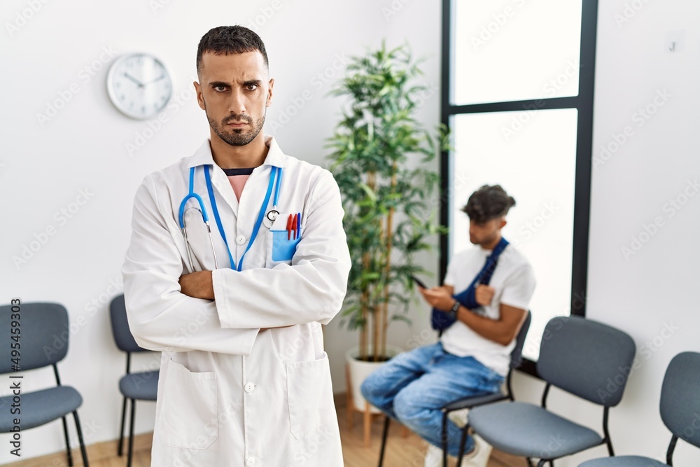Hispanic doctor man at waiting room with pacient with arm injury skeptic and nervous, disapproving expression on face with crossed arms. negative person.