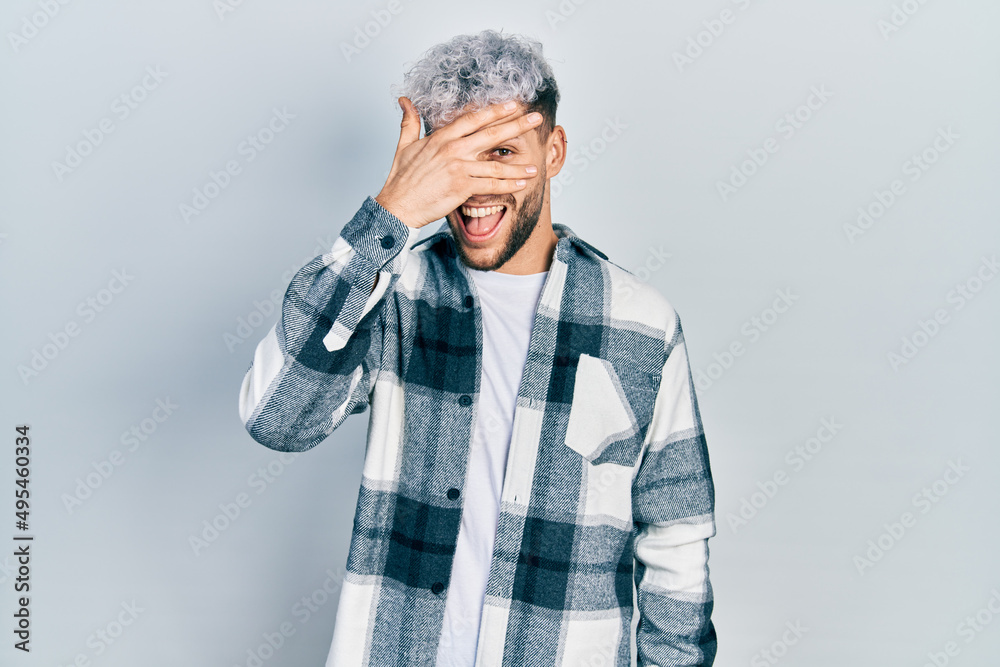 Young hispanic man with modern dyed hair wearing casual shirt peeking in shock covering face and eyes with hand, looking through fingers with embarrassed expression. Young hispanic man with modern dyed hair wearing casual shirt peeking in shock covering face and eyes with hand, looking through fingers with embarrassed expression.