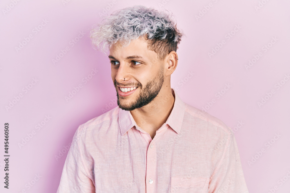 Young hispanic man with modern dyed hair wearing casual pink shirt looking to side, relax profile pose with natural face and confident smile. Young hispanic man with modern dyed hair wearing casual pink shirt looking to side, relax profile pose with natural face and confident smile.