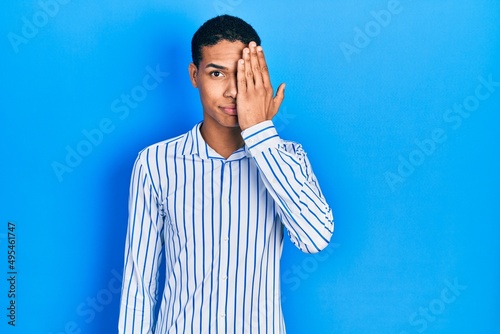 Canvastavla Young african american guy wearing casual clothes covering one eye with hand, confident smile on face and surprise emotion