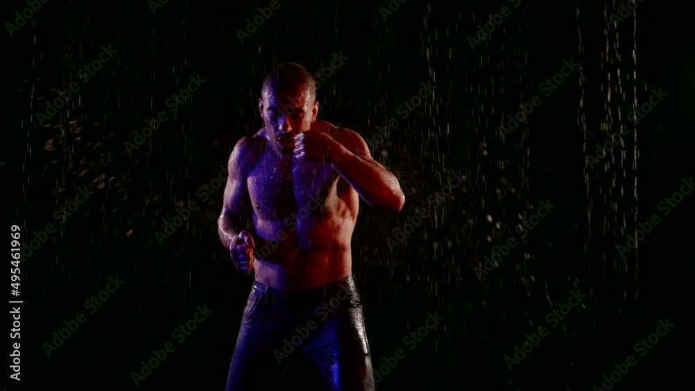 a muscular man with a bare torso strikes with hands in streams of water on a dark background. front view. the middle plan a muscular man with a bare torso strikes with hands in streams of water on a dark background. front view. the middle plan
