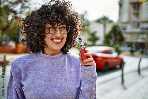 Tableau sur toile Young middle east woman smiling confident holding electronic cigarette at street