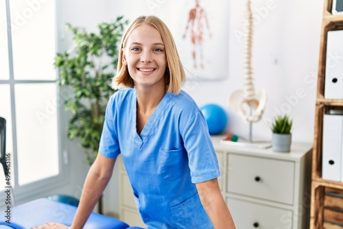 Young blonde woman wearing physiotherapist uniform standing at rehab clinic photo