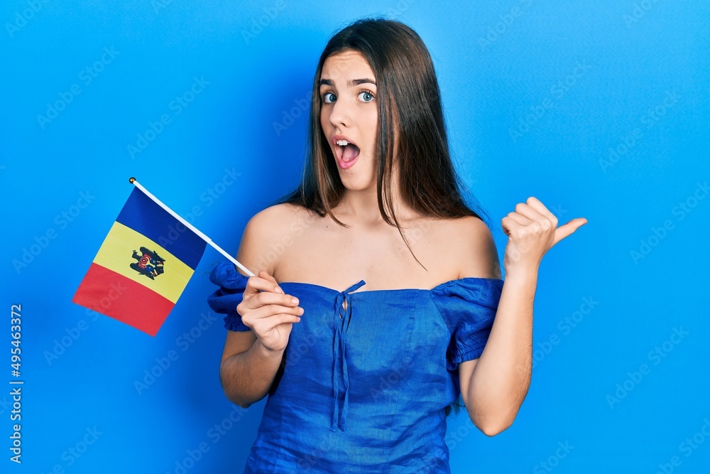 Fototapeta premium Young brunette teenager holding moldova flag pointing thumb up to the side smiling happy with open mouth