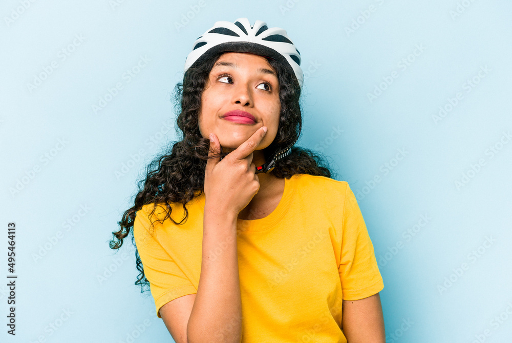 Young hispanic woman wearing a helmet bike isolated on blue background looking sideways with doubtful and skeptical expression. Young hispanic woman wearing a helmet bike isolated on blue background looking sideways with doubtful and skeptical expression.