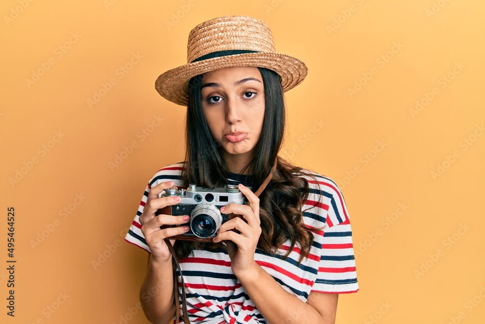 Young hispanic woman wearing summer hat holding vintage camera depressed and worry for distress, crying angry and afraid. sad expression.