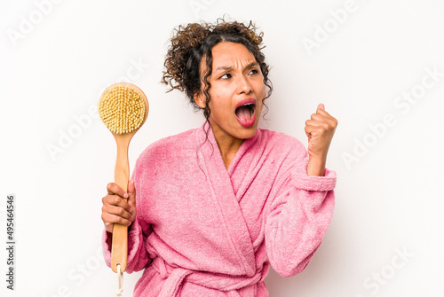 Young hispanic woman holding a back scratcher isolated on white background raising fist after a victory, winner concept.