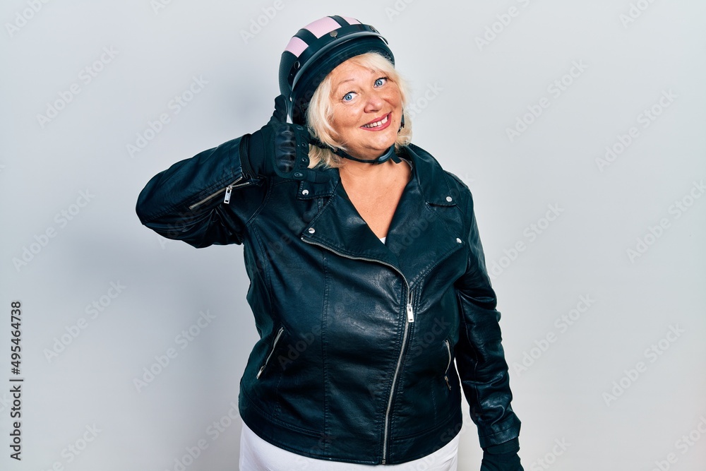 Middle age blonde woman holding motorcycle helmet smiling doing phone gesture with hand and fingers like talking on the telephone. communicating concepts. Middle age blonde woman holding motorcycle helmet smiling doing phone gesture with hand and fingers like talking on the telephone. communicating concepts.