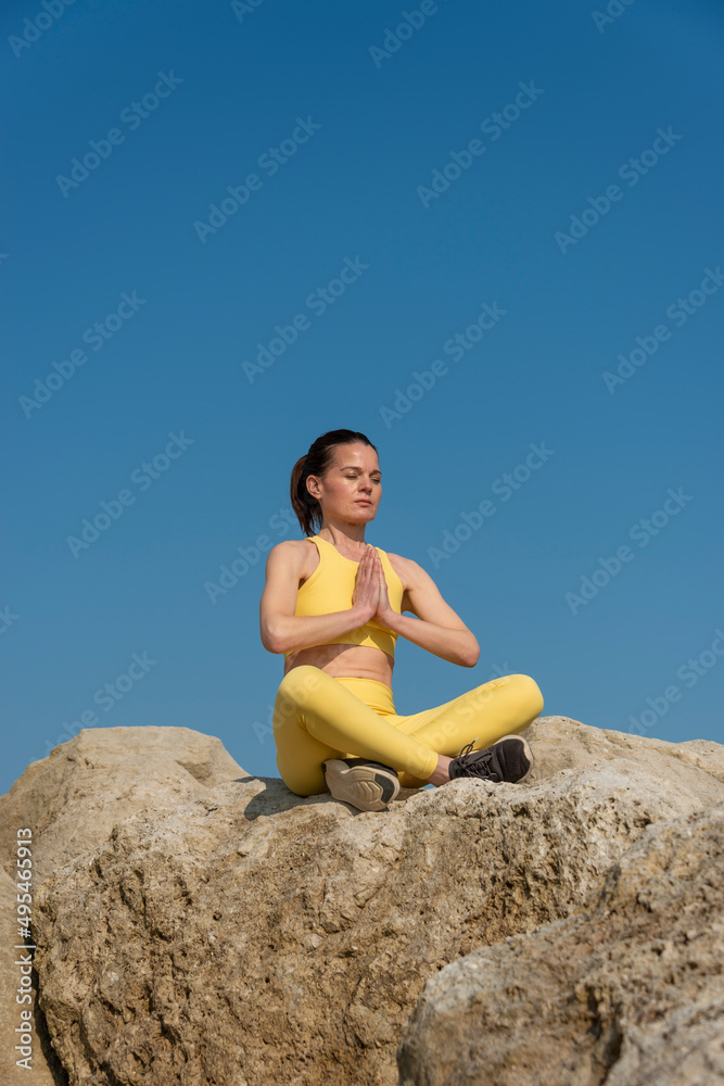 Woman doing yoga meditation sitting on rocks. Healthy mind and body.