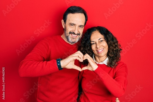 Middle age couple of hispanic woman and man hugging and standing together smiling in love doing heart symbol shape with hands. romantic concept. © Krakenimages.com