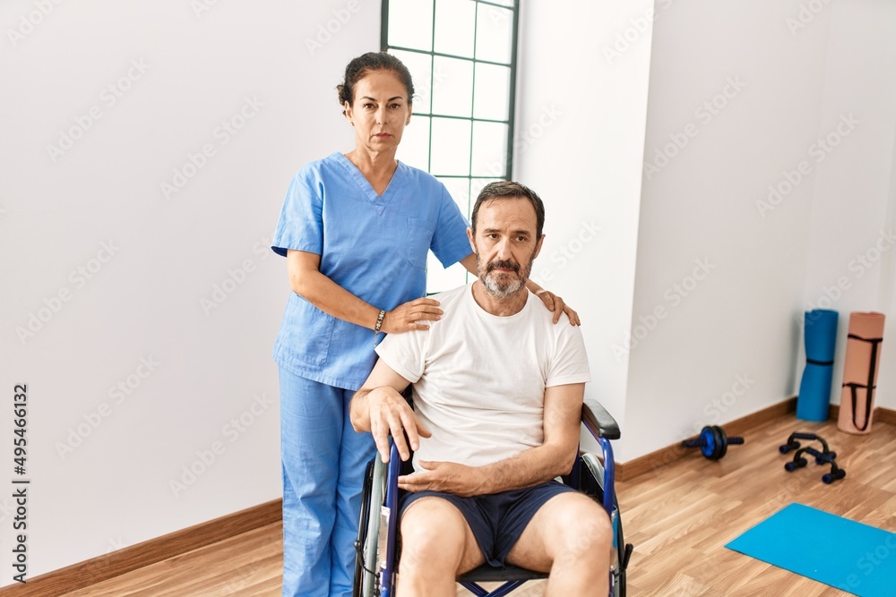 Hispanic middle age man sitting on wheelchair and nurse at rehabilitation clinic thinking attitude and sober expression looking self confident Hispanic middle age man sitting on wheelchair and nurse at rehabilitation clinic thinking attitude and sober expression looking self confident