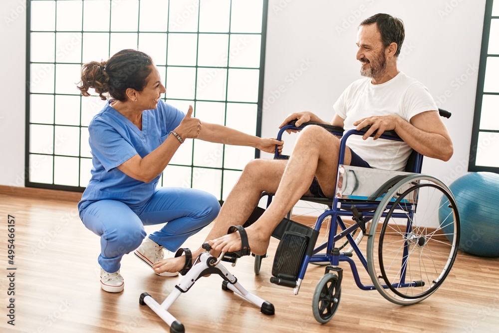 Middle age man and woman having rehab session pedaling sitting on wheelchair at physiotherapy clinic Middle age man and woman having rehab session pedaling sitting on wheelchair at physiotherapy clinic