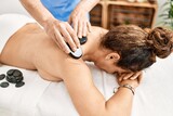 Middle age man and woman wearing therapist uniform having back massage session using hot stones at beauty center