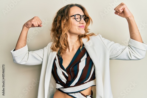 Konstfotografi Young caucasian woman wearing business style and glasses showing arms muscles smiling proud