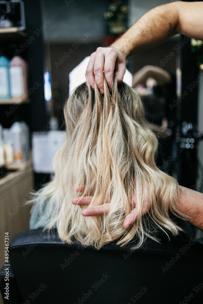 Fototapeta premium Beautiful hairstyle of woman after dyeing hair and making highlights in hair salon. She is wearing protective face mask as protection against virus pandemic.