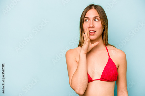 Young caucasian woman going to the beach isolated on blue background is saying a secret hot braking news and looking aside © Asier
