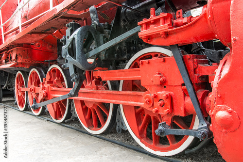Front view of an old steam locomotive. The wheels of the locomotive are red in close-up.