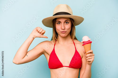 Young caucasian woman wearing a bikini and holding an ice cream isolated on blue background feels proud and self confident, example to follow.