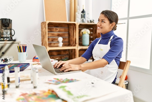 Young latin woman using laptop sitting on table at art studio