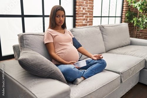 Young pregnant woman using blood pressure monitor sitting on the sofa depressed and worry for distress, crying angry and afraid. sad expression.