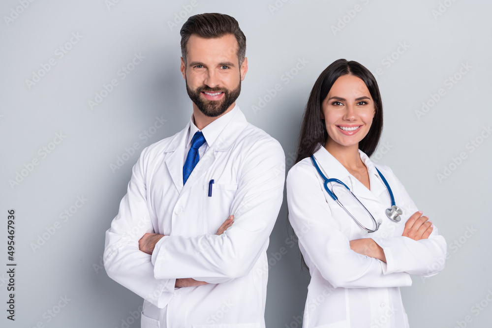 Photo of two positive professional doctors folded arms look camera isolated on grey color background Photo of two positive professional doctors folded arms look camera isolated on grey color background