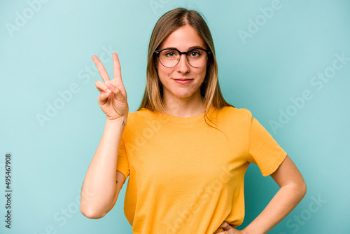 Young caucasian woman isolated on blue background joyful and carefree showing a peace symbol with fingers.